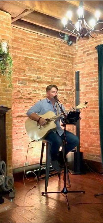 Photo of musician Scott Hoff sitting in a chair singing and playing guitar.