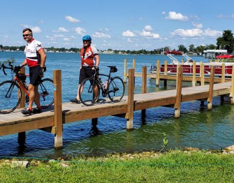 Two guys walking their bicycles across a dock on Buckeye Lake. The sky is clear and the water is a deep shade of blue.