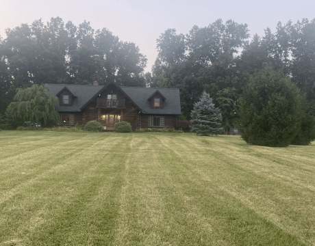 A large two-story home behind a large front yard, nestled between tall trees.