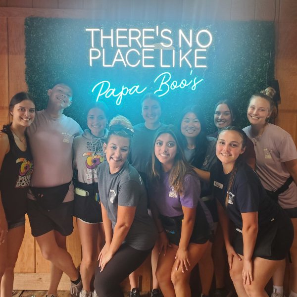 Photo of a group of people posing in front of a sign that says "There's no place like Papa Boo's"