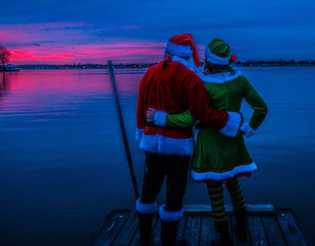 Photo of people dresses as Santa and an elf hugging as they watch the sunset over Buckeye Lake.