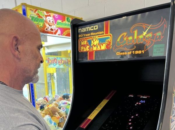 Photo of a man playing Galaga on an old arcade machine.