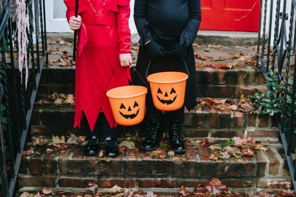 Photo of two people dressed up in Halloween costumes holding pumpkin trick or treat bins.