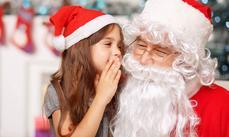 Photo of small child whispering into Santa's ear.