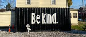 A black painted mural with words, Be Kind, in white letters.