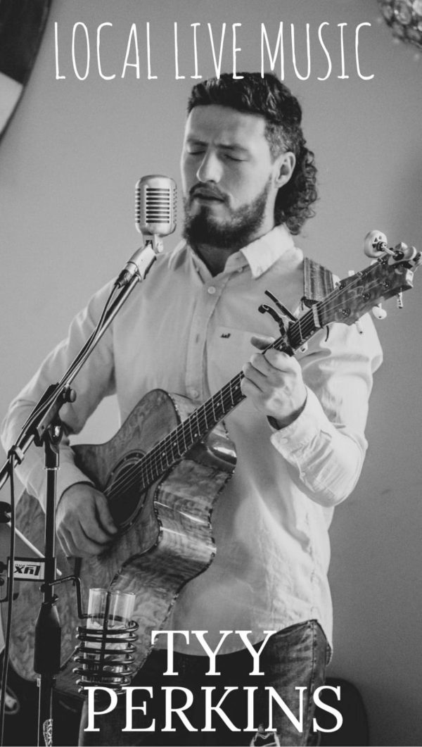 Photo of musician Tyy Perkins singing into a microphone while playing guitar.