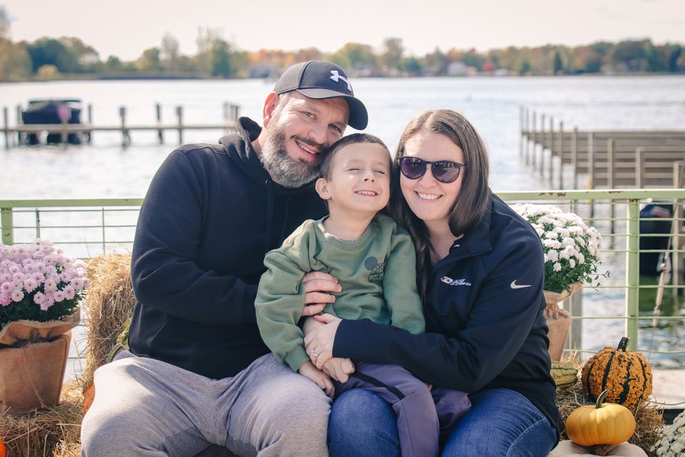 Photo of a family sitting and smiling on a hay bail in front of a lake.