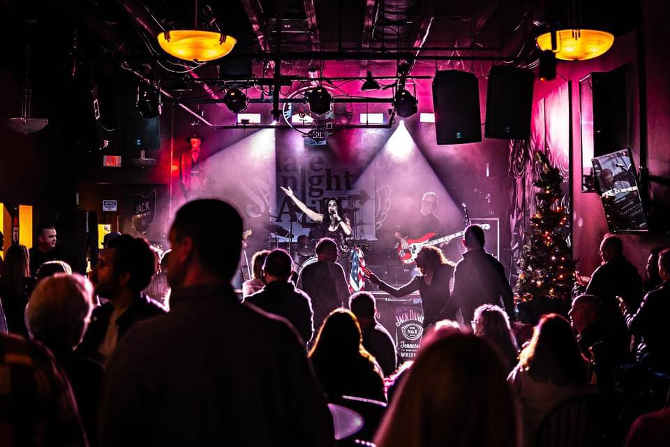 Photo of the band Late Night Alibi playing on a stage in front of a crowd with purple lights