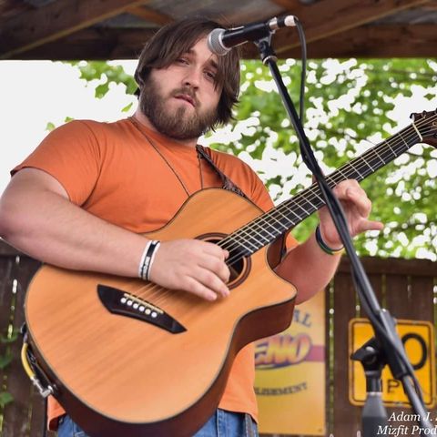 Photo of musician Randy Gleason posing with a guitar behind the microphone