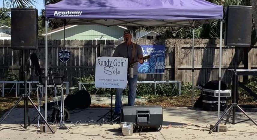 Image of musician Randy Goin Solo singing and playing guitar under a tent