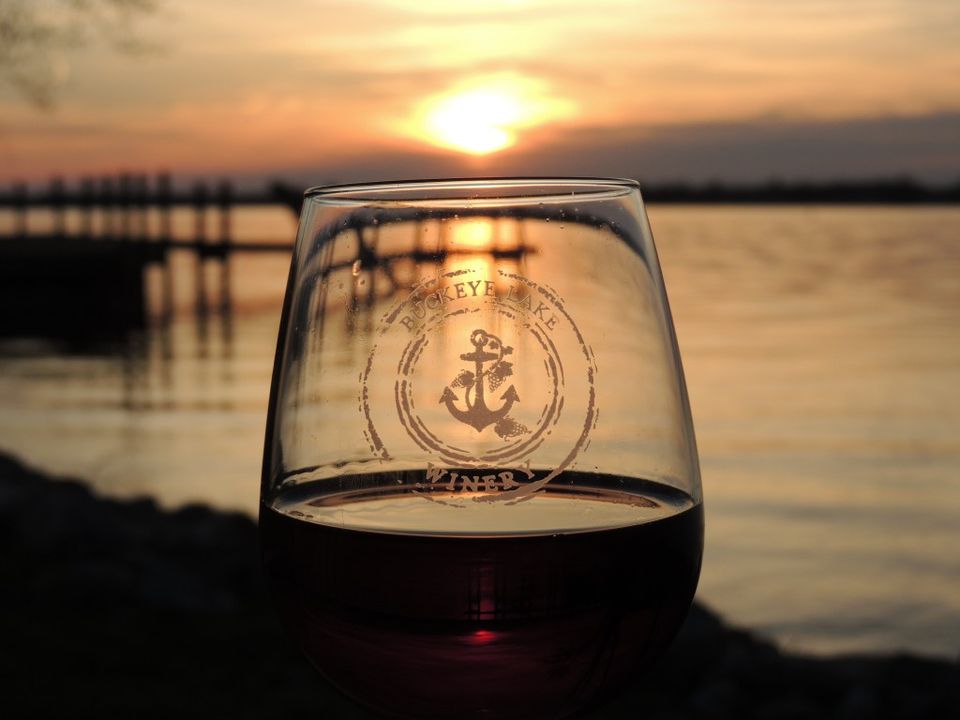 Photo of a Buckeye Lake Winery wine glass in front of a sunset on a lake