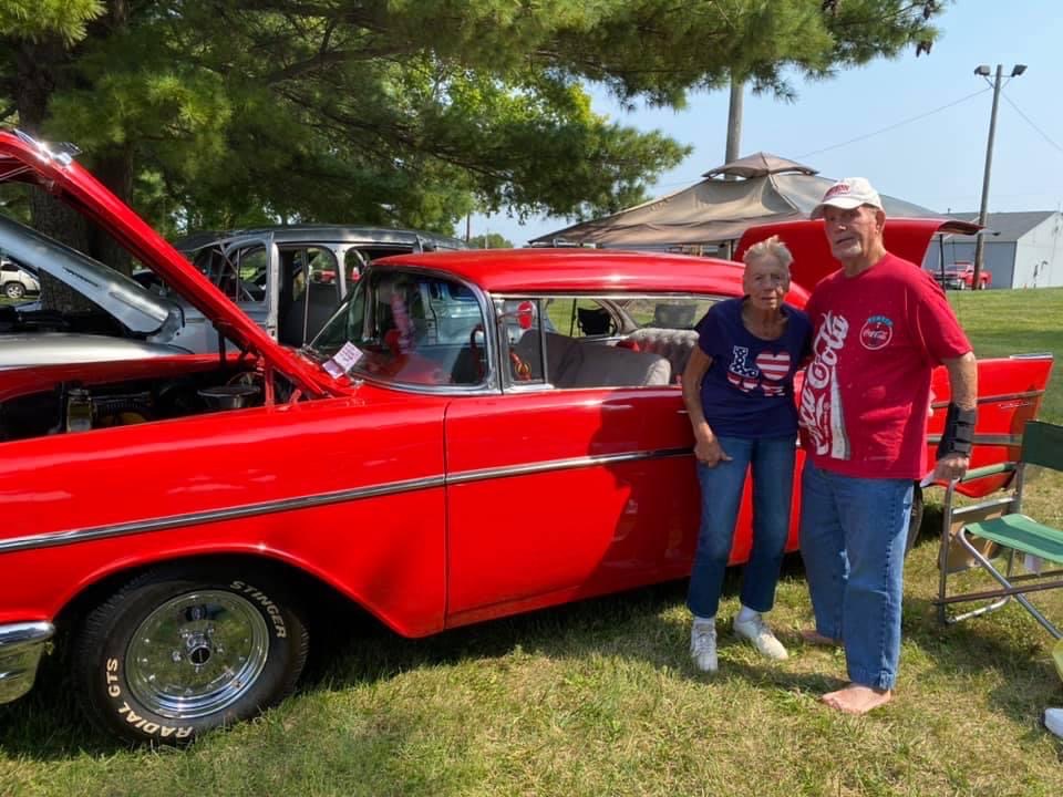 Photo of a couple posed beside an old red car