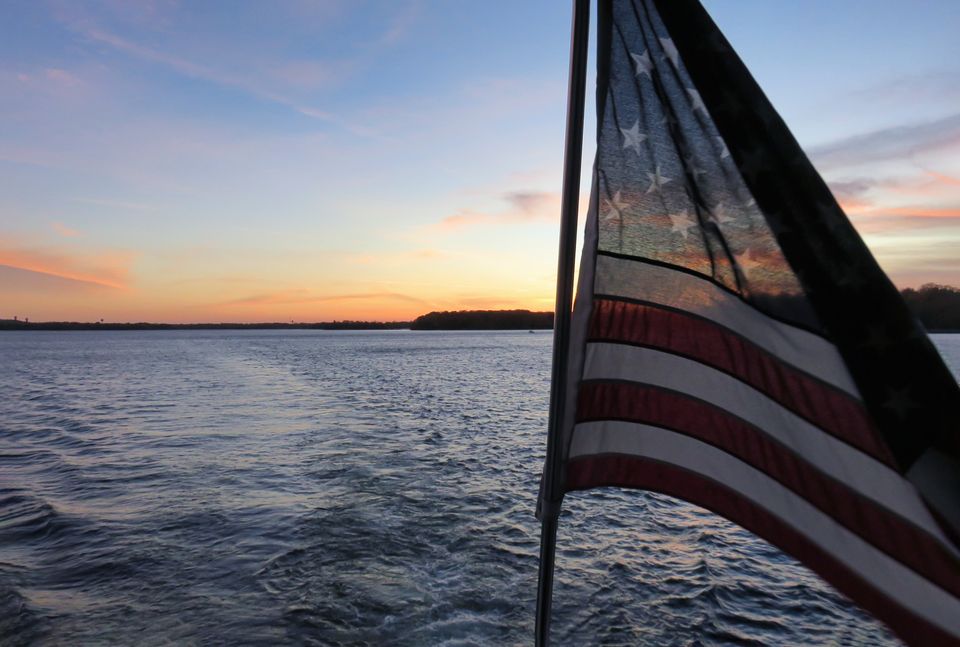 Photo of an American flag swaying in the wind in front of a sunset on a lake