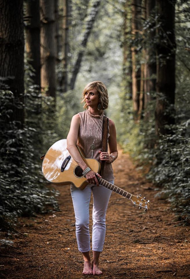 A girl in the woods holding a guitar